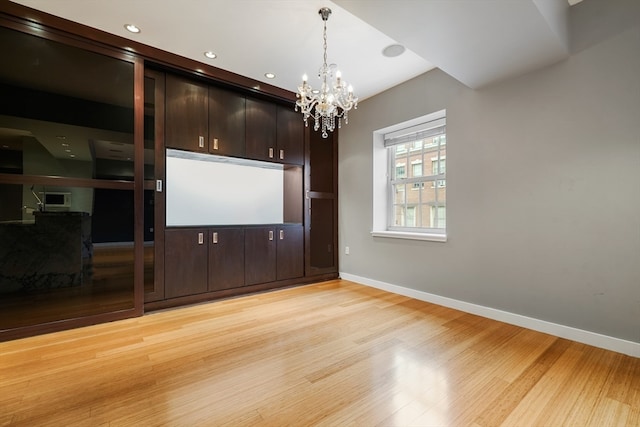 spare room featuring a notable chandelier and light wood-type flooring