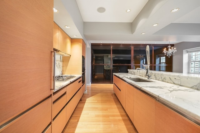 kitchen with light stone counters, stainless steel gas cooktop, a tray ceiling, light wood-type flooring, and pendant lighting