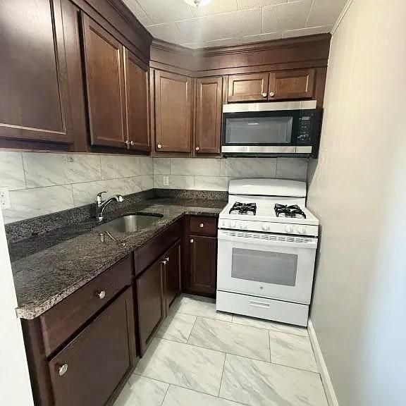 173 County St, Fall River, MA 02723 - kitchen featuring stainless steel microwave, white gas range, light marble finish flooring, dark stone countertops, and dark brown cabinetry