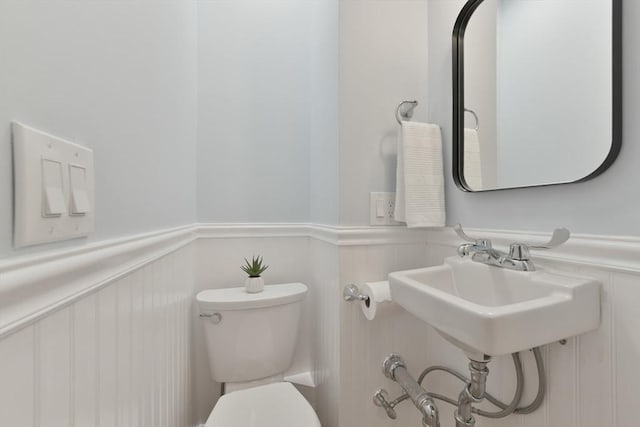 half bath with toilet, a decorative wall, and a wainscoted wall