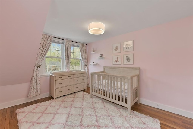 bedroom featuring baseboards, a crib, and wood finished floors