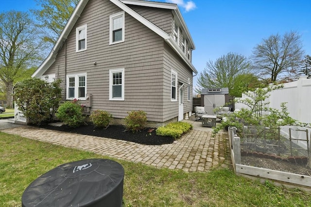 view of side of home with a vegetable garden, fence, a patio, an outdoor structure, and a storage shed