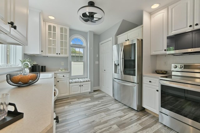 kitchen with glass insert cabinets, light countertops, white cabinetry, and stainless steel appliances