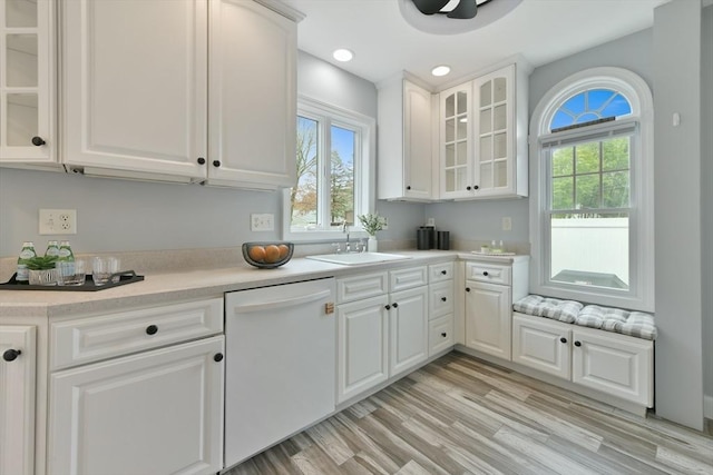 kitchen featuring a sink, dishwasher, white cabinetry, light countertops, and glass insert cabinets