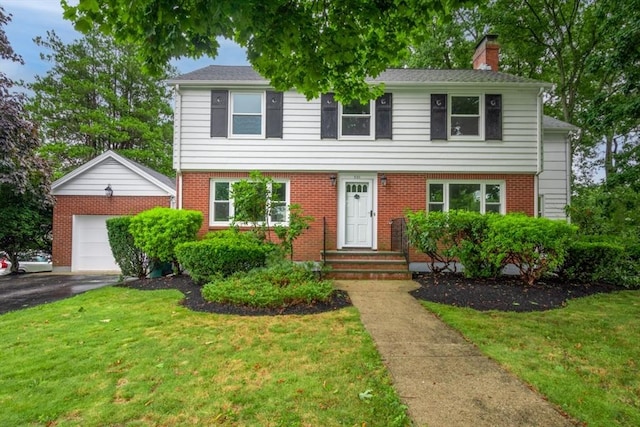 colonial inspired home with a chimney, an outdoor structure, aphalt driveway, and a front lawn