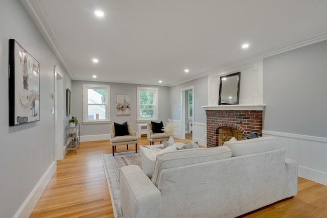 living area with recessed lighting, radiator heating unit, a brick fireplace, crown molding, and light wood-type flooring