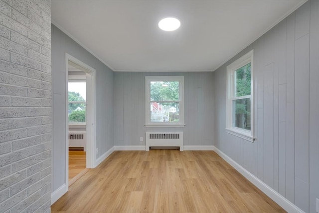empty room with radiator, crown molding, light wood finished floors, and a healthy amount of sunlight
