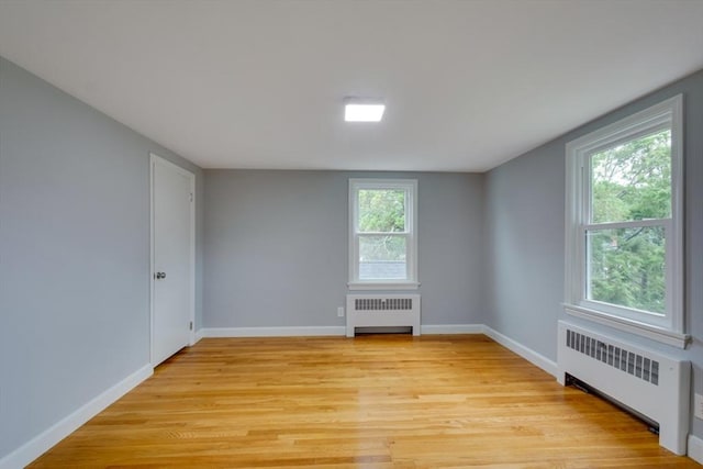 empty room with radiator, light wood finished floors, and baseboards
