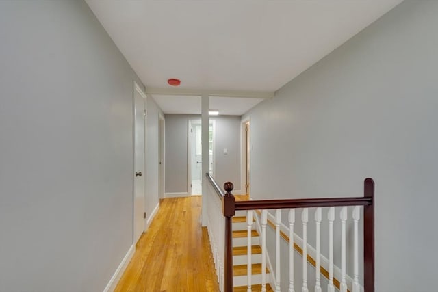 hallway with baseboards, an upstairs landing, and light wood-style flooring