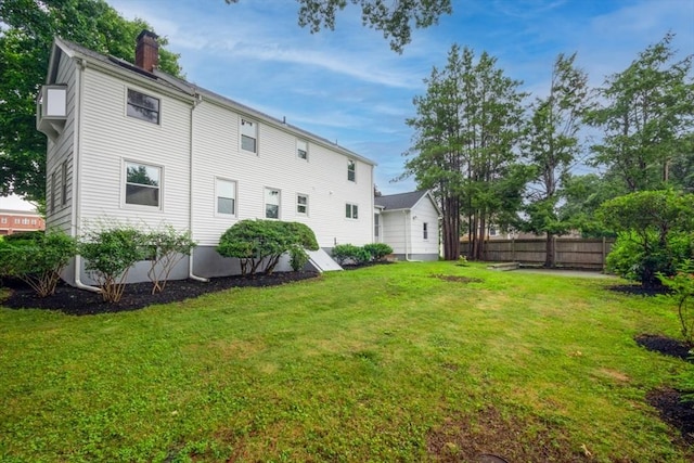 rear view of property featuring fence, a chimney, and a lawn
