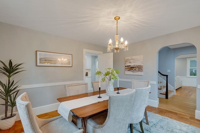 dining space featuring stairway, a chandelier, arched walkways, and baseboards