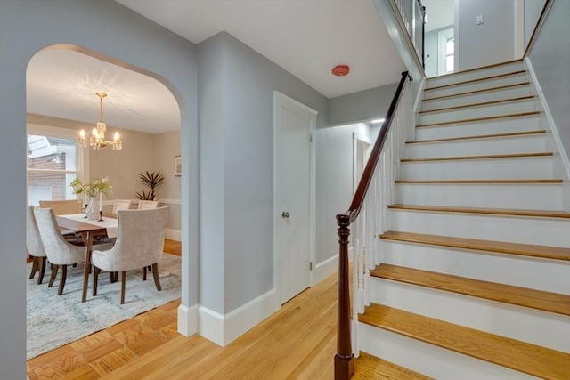staircase with an inviting chandelier, arched walkways, baseboards, and wood finished floors