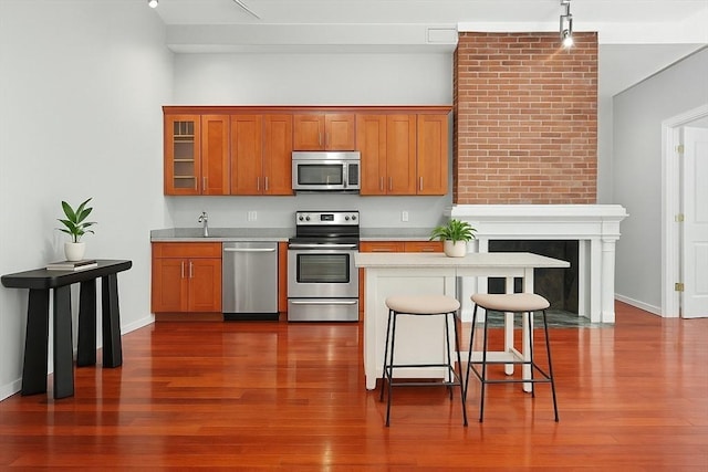 kitchen with dark wood-style flooring, appliances with stainless steel finishes, light countertops, a kitchen breakfast bar, and brown cabinetry