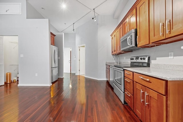 kitchen with a towering ceiling, baseboards, dark wood-type flooring, brown cabinets, and stainless steel appliances