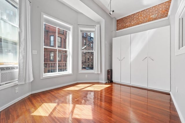 unfurnished bedroom featuring baseboards, multiple windows, cooling unit, and wood finished floors
