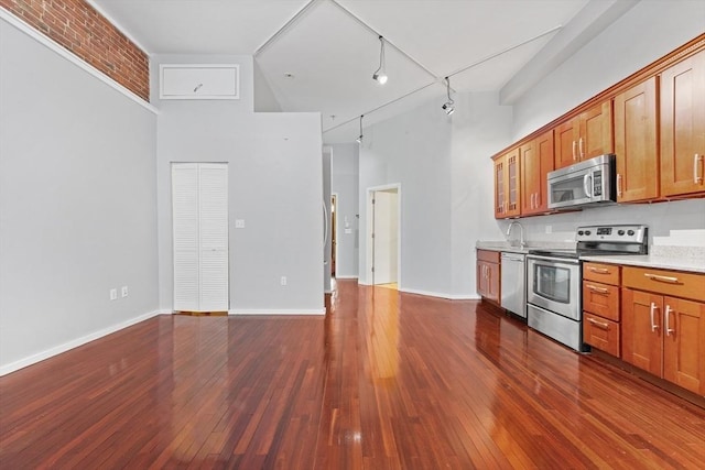 kitchen with a high ceiling, dark wood-style floors, light countertops, brown cabinets, and appliances with stainless steel finishes