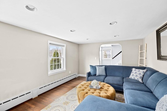living room featuring stairs, wood finished floors, arched walkways, a baseboard heating unit, and recessed lighting