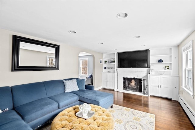 living area featuring recessed lighting, a fireplace with flush hearth, dark wood finished floors, arched walkways, and baseboard heating