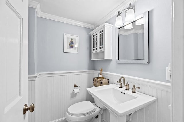 half bath featuring toilet, a sink, ornamental molding, and wainscoting