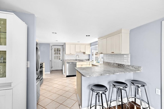 kitchen featuring tasteful backsplash, light tile patterned floors, stainless steel dishwasher, a sink, and a peninsula