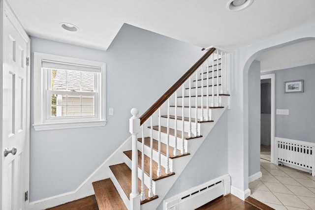 stairs featuring baseboards, tile patterned floors, arched walkways, radiator heating unit, and baseboard heating