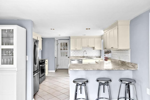 kitchen with a breakfast bar, decorative backsplash, a sink, a peninsula, and appliances with stainless steel finishes