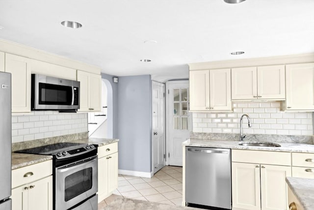 kitchen featuring light tile patterned floors, decorative backsplash, a sink, light stone counters, and appliances with stainless steel finishes
