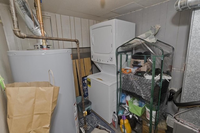 laundry room with stacked washer / drying machine, wooden walls, water heater, and a textured ceiling