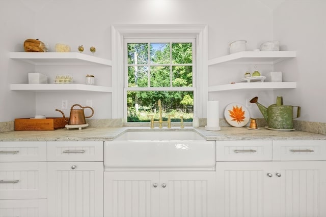 kitchen with light stone countertops, white cabinetry, and sink