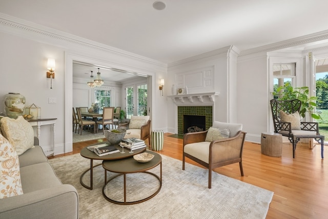 living room with light hardwood / wood-style flooring, a tile fireplace, an inviting chandelier, and crown molding