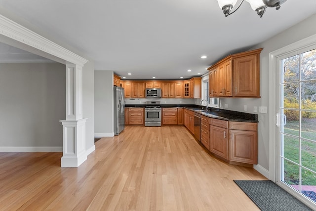 kitchen with dark stone counters, decorative columns, ornamental molding, light hardwood / wood-style floors, and stainless steel appliances