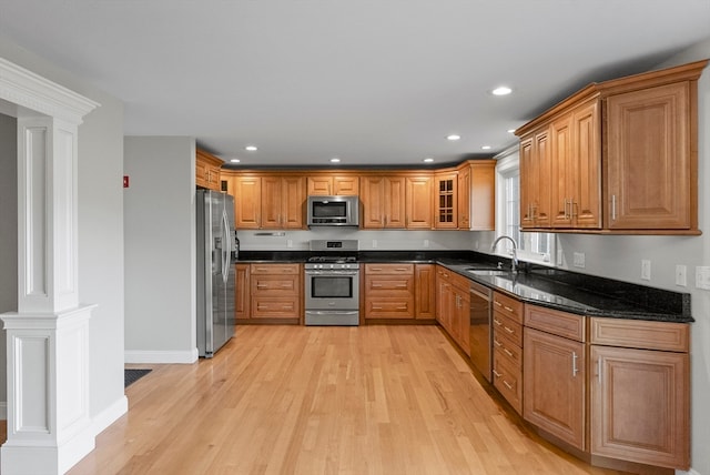 kitchen featuring ornate columns, stainless steel appliances, dark stone counters, sink, and light hardwood / wood-style floors