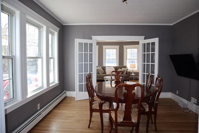 dining room with baseboards, baseboard heating, ornamental molding, and light wood-style floors