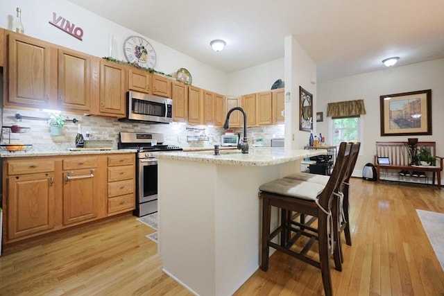 49 Branch St Unit 49, Clinton, MA 01510 - kitchen featuring appliances with stainless steel finishes, light wood finished floors, decorative backsplash, a breakfast bar area, and light stone countertops