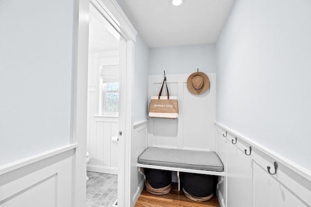 mudroom with light wood finished floors, wainscoting, and a decorative wall