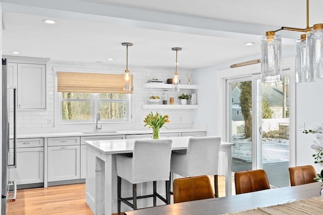 kitchen featuring decorative light fixtures, open shelves, light countertops, a sink, and plenty of natural light