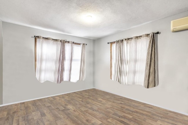 empty room with baseboards, a textured ceiling, wood finished floors, and a wall mounted AC