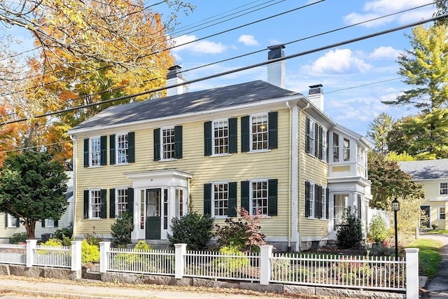 colonial inspired home featuring a chimney and a fenced front yard