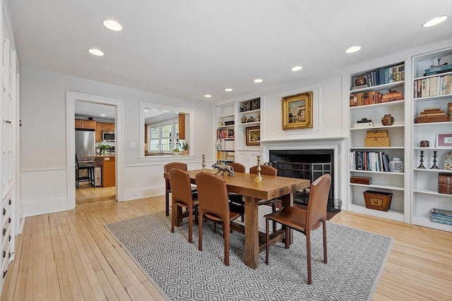 dining area featuring light wood finished floors, a fireplace, built in shelves, and recessed lighting