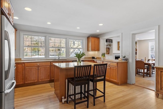 kitchen with light wood-type flooring, stainless steel fridge, brown cabinets, and a sink