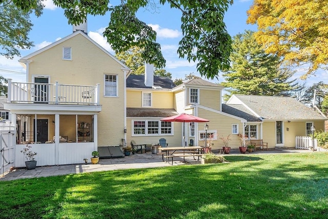 rear view of house with a patio, a lawn, a chimney, and a balcony