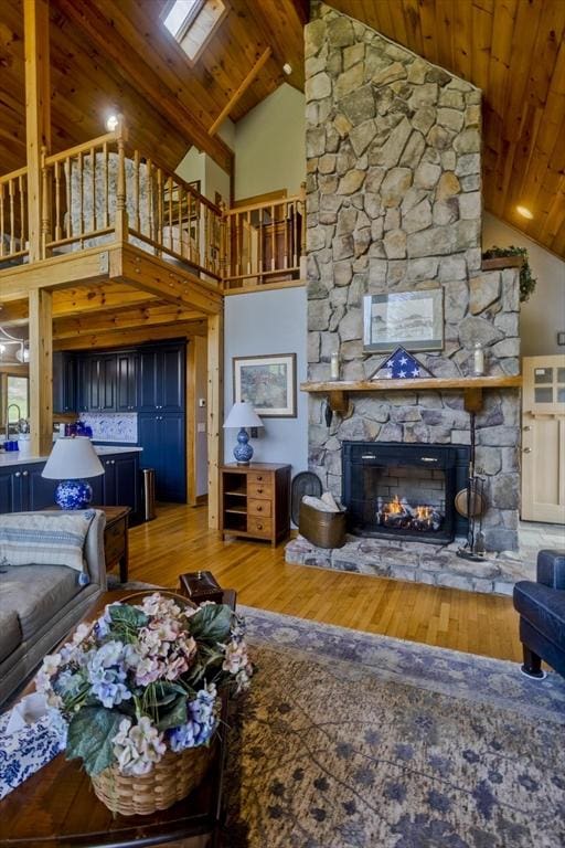 living room with beam ceiling, wood finished floors, a stone fireplace, high vaulted ceiling, and wood ceiling