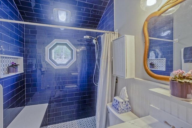 full bath with toilet, a tile shower, and a wainscoted wall
