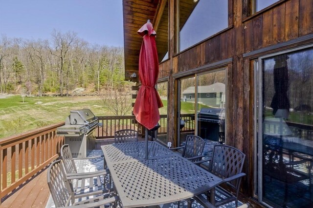 deck featuring outdoor dining area, area for grilling, and a forest view