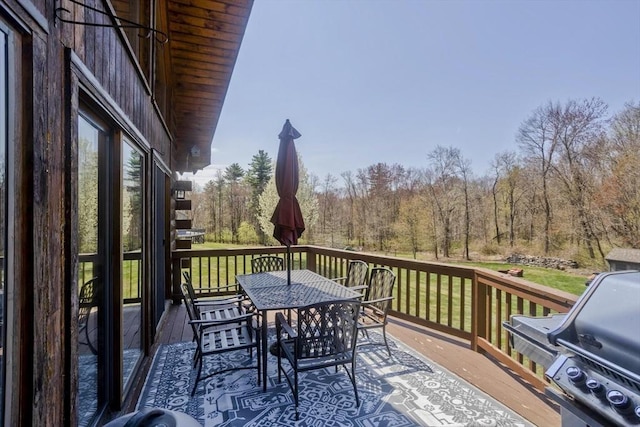 deck featuring a lawn, a forest view, outdoor dining space, and area for grilling