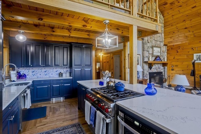 kitchen featuring wooden walls, a sink, a stone fireplace, stainless steel appliances, and blue cabinets