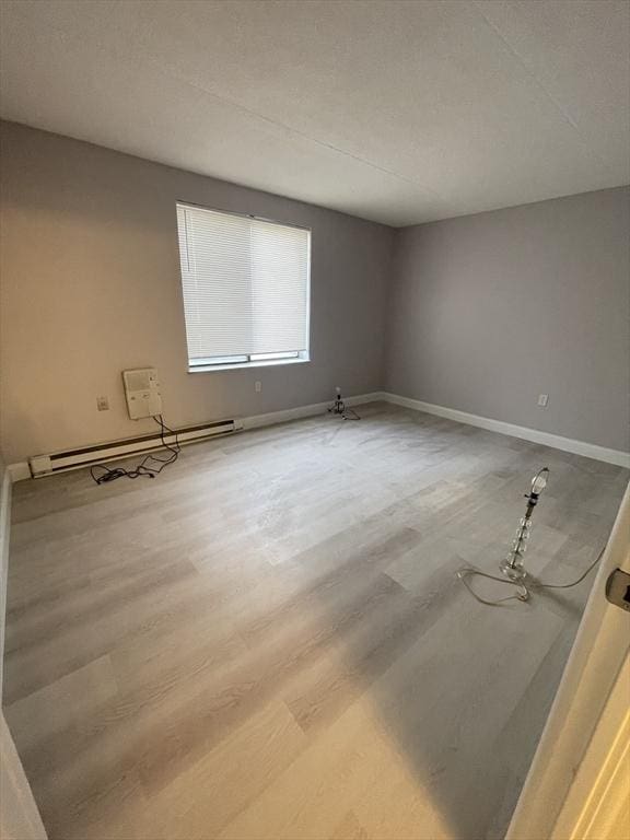 empty room with hardwood / wood-style flooring and a baseboard heating unit