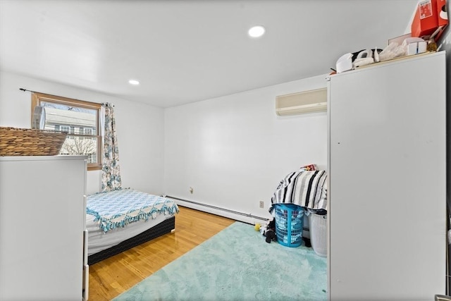 bedroom featuring hardwood / wood-style floors, a baseboard radiator, and a wall unit AC