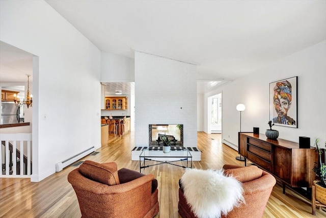 living room featuring a fireplace, a baseboard radiator, a chandelier, and light wood-type flooring