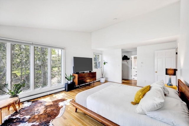 bedroom featuring vaulted ceiling, baseboard heating, and light hardwood / wood-style flooring